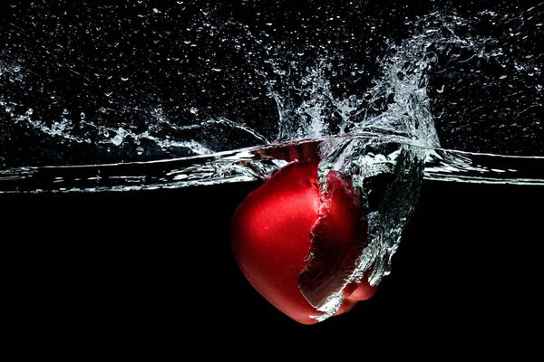 close up view of red apple falling into water isolated on black