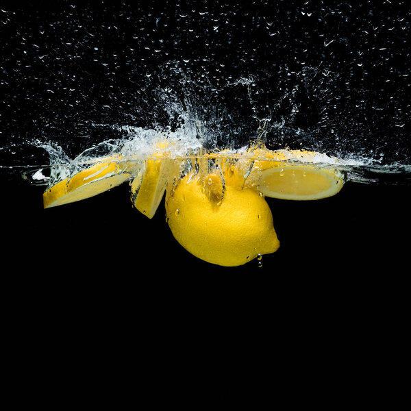 close up view of fresh lemon pieces in water with splashes isolated on black