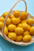 zralé žluté citrony v proutěném koši na modrém pozadí