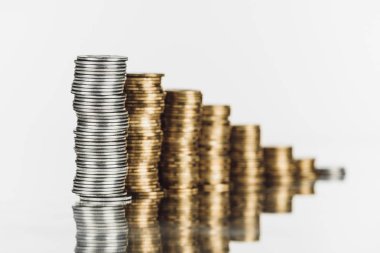 selective focus of stacked silver and golden coins on surface with reflection isolated on white clipart