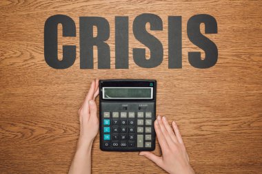 cropped view of female hands near calculator with one hundred thousand on display, and word crisis on wooden desk clipart