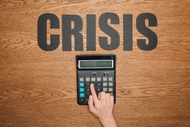 cropped view of female hand on calculator with one hundred thousand on display, and word crisis on wooden desk clipart