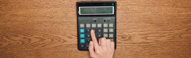 partial view of female hand on calculator with one hundred thousand on display on wooden desk, panoramic shot clipart