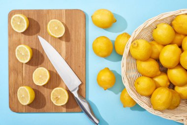 Tahta kesme tahtasındaki limonları, mavi arka plandaki bıçakla hasır sepetteki bütün limonların yakınındaki limonları görüyor.