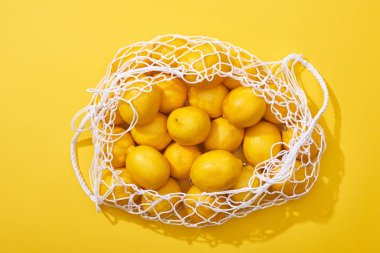 top view of fresh ripe whole lemons in eco string bag on yellow background clipart
