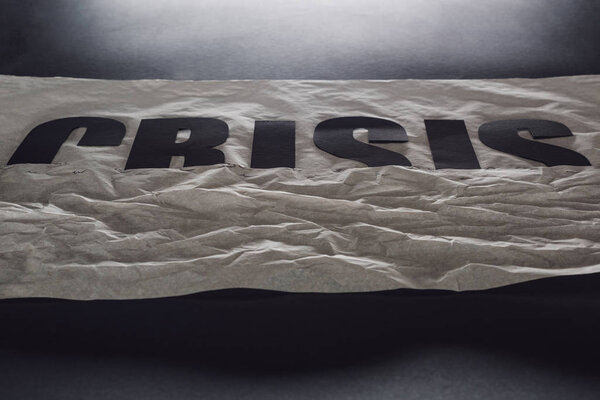 black word crisis immersed in paper symbolizing water on black background with lighting