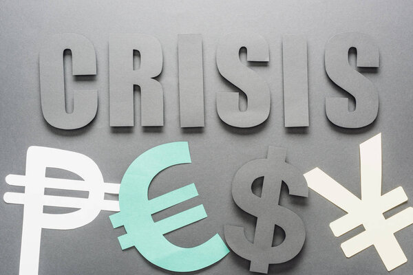 top view of word crisis near peso, euro, dollar and yen symbols on grey background with shadow