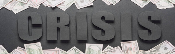 top view of word crisis near scattered dollar banknotes on black background with shadows, panoramic shot