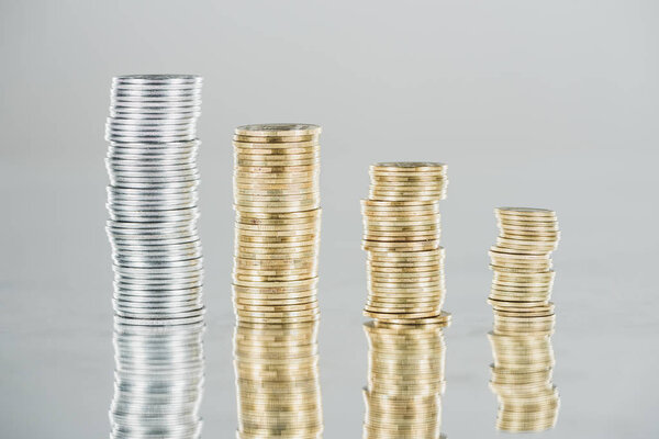 stacks of silver and golden coins on surface with reflection isolated on grey