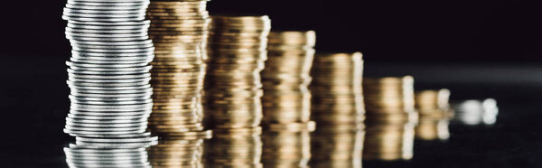 selective focus of stacked silver and golden coins on surface with reflection isolated on black, panoramic shot