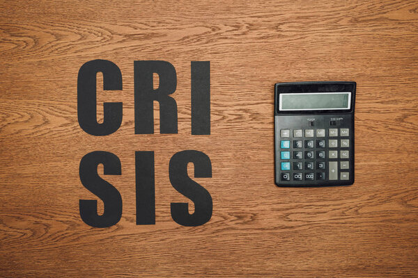 top view of black paper cut word crisis near calculator on wooden desk