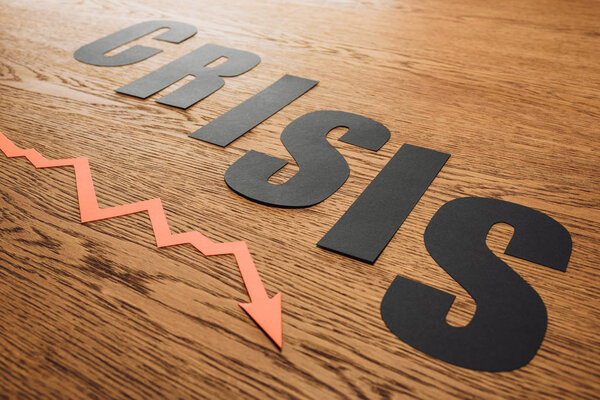 black paper cut word crisis near recession arrow on wooden surface with lighting