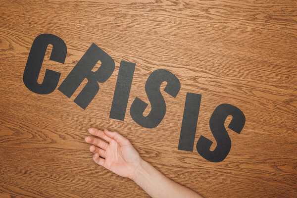 cropped view of female hand near black paper cut word crisis on wooden floor