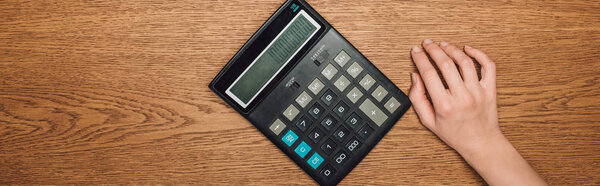 частичный вид женской руки рядом с калькулятором со ста тысячами на деревянном столе, панорамный снимок
