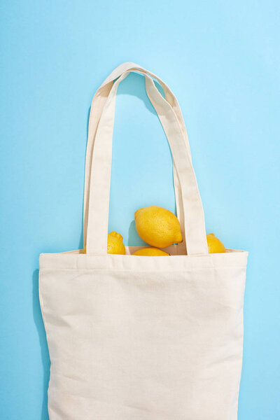 top view of ripe yellow lemons in cotton eco bag on blue background