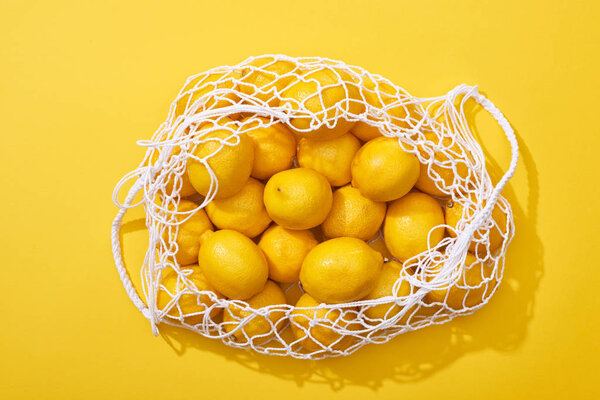 top view of fresh ripe whole lemons in eco string bag on yellow background