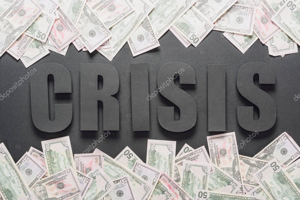 top view of word crisis near scattered dollar banknotes on black background with shadows