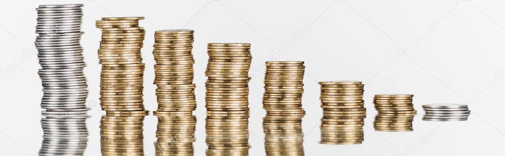 panoramic shot of stacked silver and golden coins on surface with reflection isolated on white