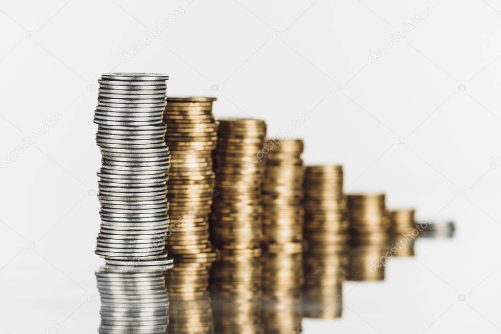selective focus of stacked silver and golden coins on surface with reflection isolated on white