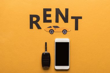 Boş ekranlı akıllı telefonun üst görünümü, araba anahtarı, kağıt kesme otomatiği ve turuncu arkaplanda siyah kira harfleri