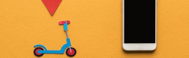 Kağıt kesiği scooter 'ın üst görüntüsü, akıllı telefonun yanında konum işareti turuncu arkaplanda boş ekran, panoramik çekim