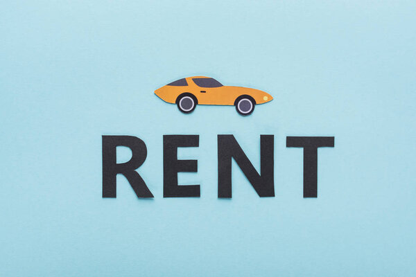 top view of paper cut sports car and black rent lettering on blue background