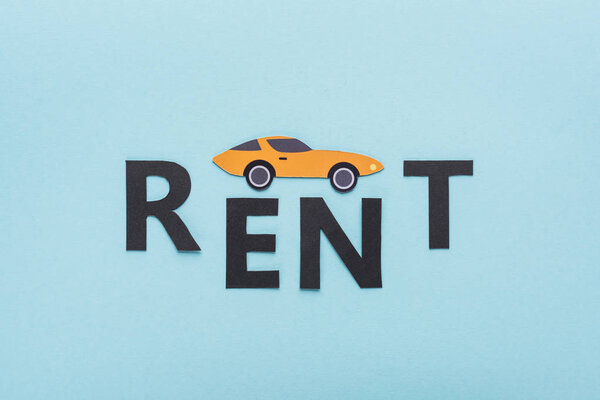 top view of paper cut sports car and black rent lettering on blue background