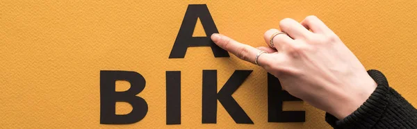 cropped view of woman pointing with finger at bike lettering on orange background