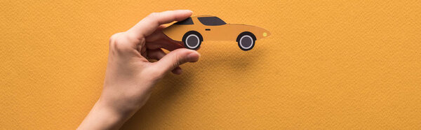 cropped view of woman holding paper cut sports car on orange background, panoramic shot