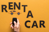 cropped view of woman holding key near paper cut rent a car lettering on orange background