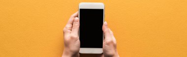Turuncu arka planda boş ekranlı akıllı telefonu olan bir kadının panoramik görüntüsü.