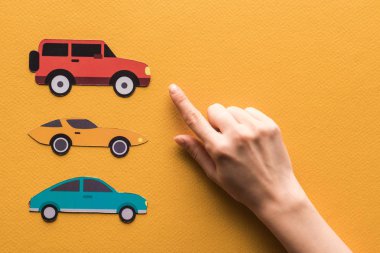 cropped view of woman pointing with finger at paper cars on orange background clipart