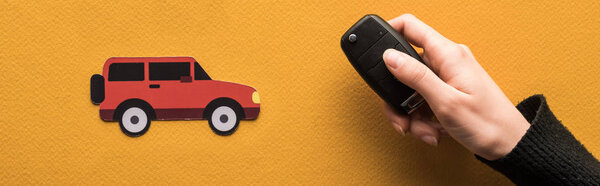 обрезанный вид женщины с ключом рядом с бумагой разрезать автомобиль на оранжевом фоне, панорамный снимок
