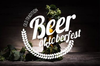 Şişe içinde taze bira, yeşil zıpla ahşap yüzeyde, karanlıkta eski geleneksel bira Ekim Festivali illüstrasyonuyla.
