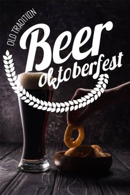 Bir kadının ahşap masada bir bardak biranın yanında kızarmış soğan halkası ve beyaz eski gelenek bira Oktoberfest yazısıyla görüntülenmiş.