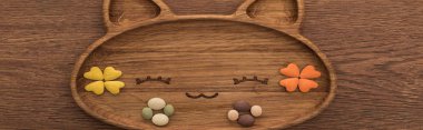 top view of feline dry pet food and vitamins in cute cat shape plate on wooden table, panoramic shot clipart