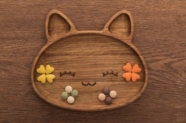 top view of feline dry pet food and vitamins in cute cat shape plate on wooden table clipart