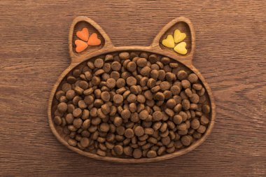 Kedi maması ve kedi şekilli tabakta vitaminler ahşap masada.