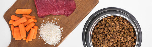 top view of dry pet food and raw meat, rice, carrot on wooden cutting board isolated on white, panoramic shot