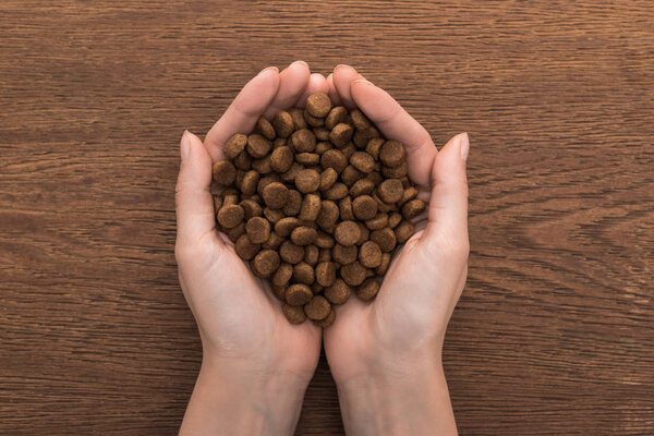 cropped view of woman holding dry pet food on wooden table