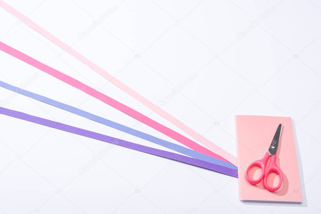 high angle view of notebook, scissors and paper strips on white background 