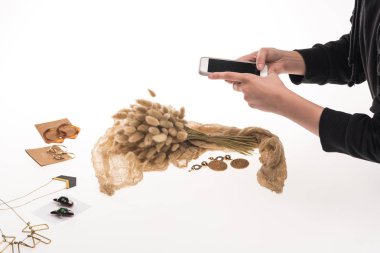 Fotoğrafçının flora ile kompozisyon ve beyaz telefon ile mücevher çekerken çekilmiş görüntüsü.