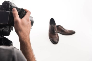 Erkek fotoğrafçının beyaz üzerine erkek ayakkabılarının ticari fotoğraf çekimini yaparken çekilmiş görüntüsü.
