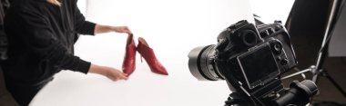 Ticari fotoğrafçının beyaz, panoramik bir karede kırmızı topuklu kadın ayakkabısının ticari fotoğraf çekimini yaparken çekilmiş görüntüsü.