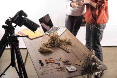 cropped view of two commercial photographers working with accessories, digital camera, laptop and smartphone clipart