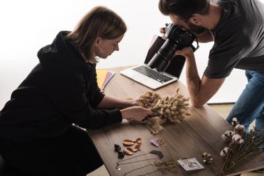 two commercial photographers take picture of composition with flora and jewelry on digital camera clipart