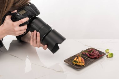 Ticari fotoğrafçılık için yemek kompozisyonu yapan ve beyaz kamerada fotoğraf çeken kadın fotoğrafçı görüntüsü.