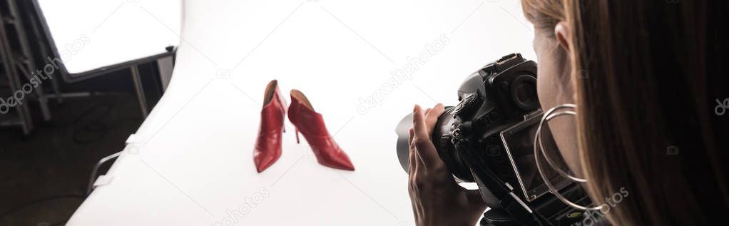 cropped view of commercial photographer making commercial photo shoot of female red heel shoes on white, panoramic shot