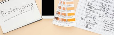 Web sitesi tasarım şablonu, renk paleti ve bej arkaplan üzerinde prototip harfleri olan not defteri yakınlarındaki akıllı telefonun üst görünümü, panoramik çekim