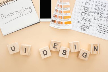 Web sitesi tasarım şablonu, renk paleti ve not defteri yakınlarındaki akıllı telefonun üst görünümü üzerinde bej arkaplan üzerinde ui tasarımı harfi olan tahta blokların üzerinde prototip yazılıdır.